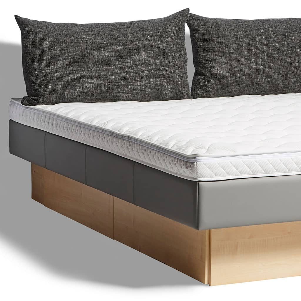 L’angle d’un lit à eau Modulex avec deux coussins de tête gris, contour anthracite et socle en bois clair.