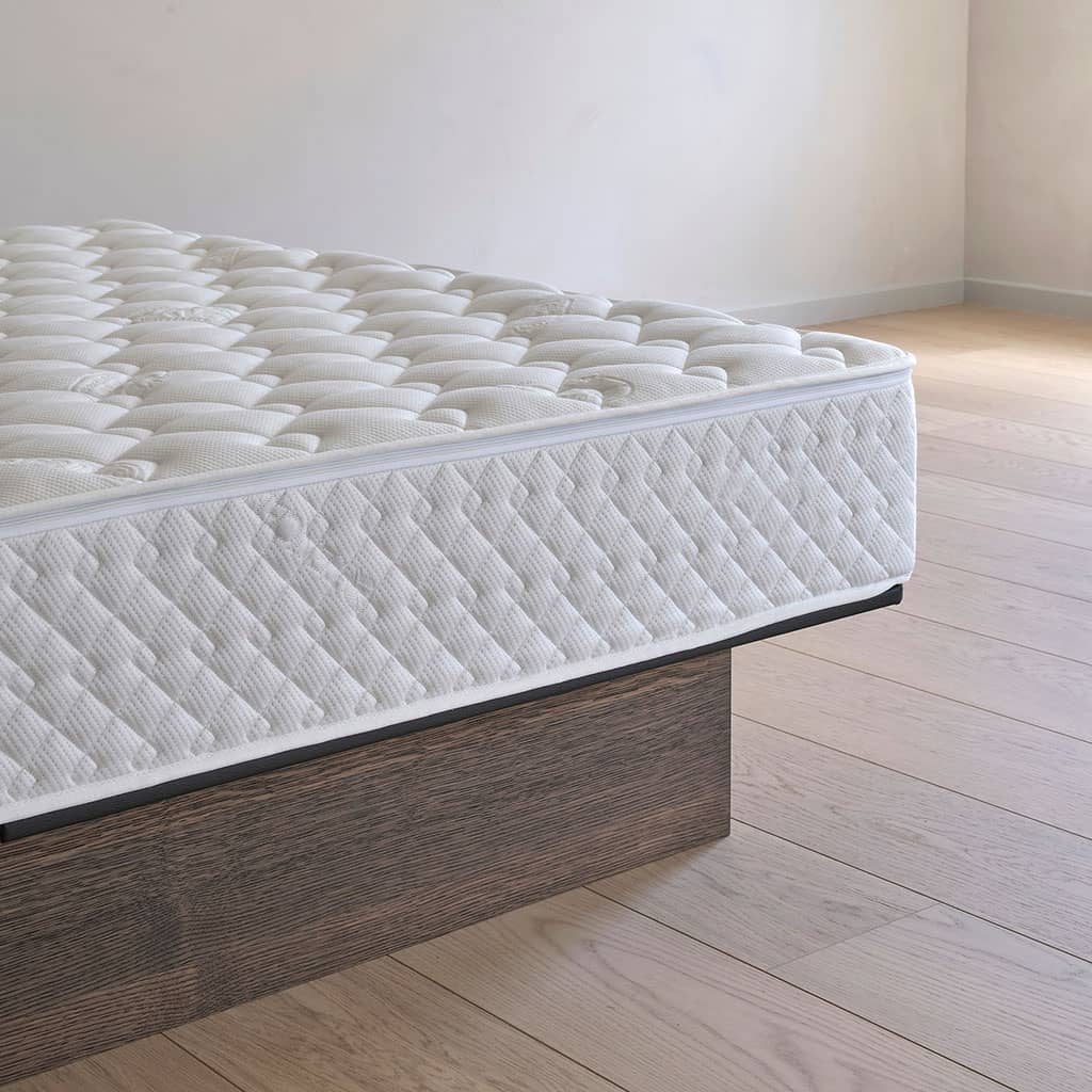 L’angle d’un lit à eau : le revêtement matelassé blanc et sa fermeture éclair, posé sur un socle en chêne foncé.