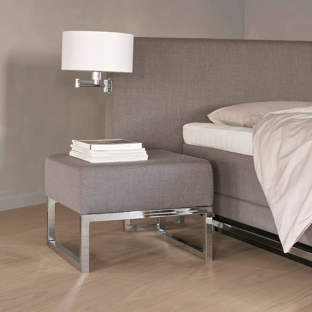 Pouf Akva Vega en chevet à côté d'un lit Vega, livres posés sur l'assise