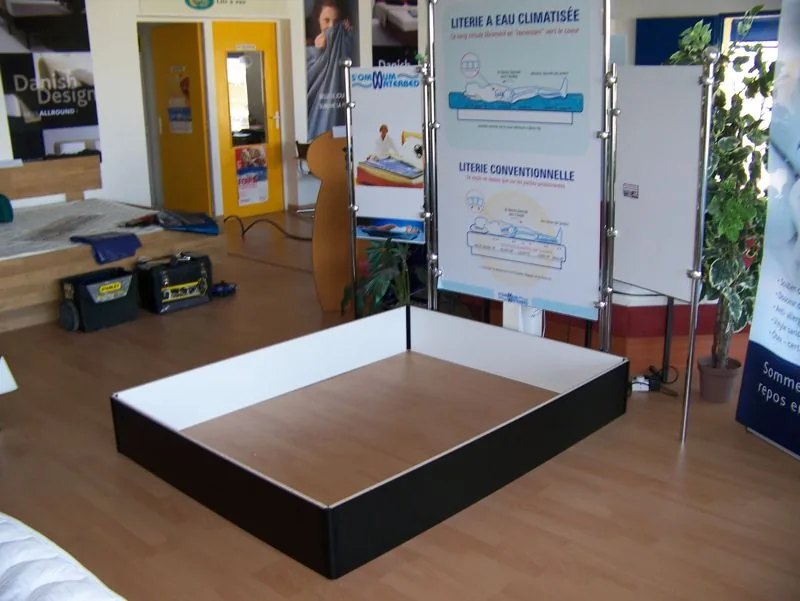 Socle de lit à eau assemblé au showroom : caisse noire à fond clair, vue d'ensemble
