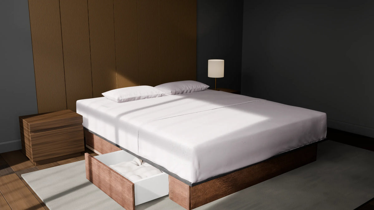 Un lit a eau fait, dans une chambre sombre : housse blanche tendue, deux oreillers, socle en bois dont un tiroir est ouvert.