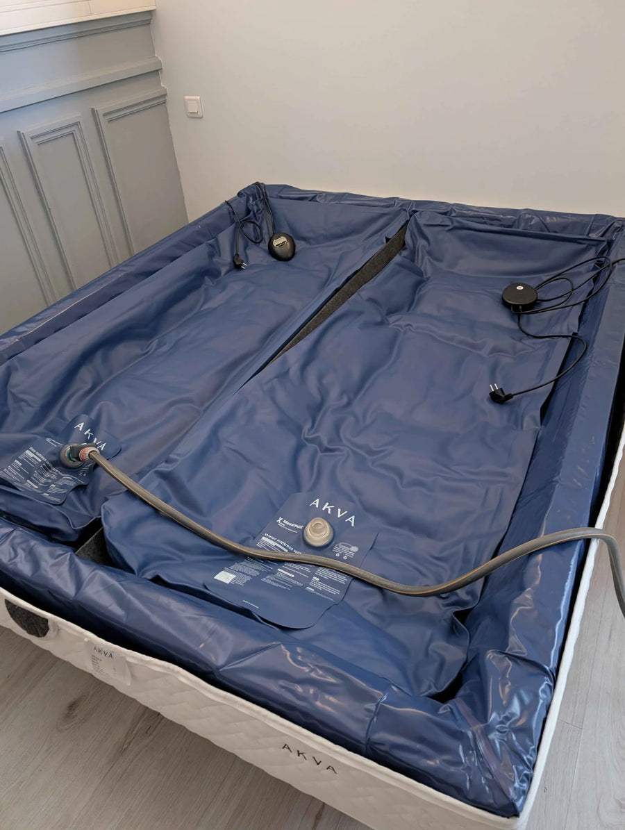 Exemple en lit duo : deux matelas à eau Akva en vinyle bleu marine posés dans leur cadre en mousse, le tuyau de remplissage branché sur la valve, les boîtiers de chauffage et leurs câbles sur le dessus.